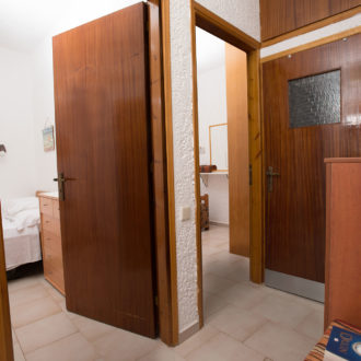 A simple apartment interior with wooden doors, tiled floors, and a glimpse into the bedroom area