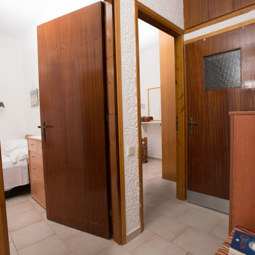 A simple apartment interior with wooden doors, tiled floors, and a glimpse into the bedroom area