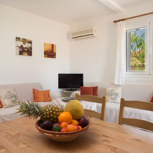 Bright apartment living room with two sofas, a dining table, wall art, and a window to greenery outside