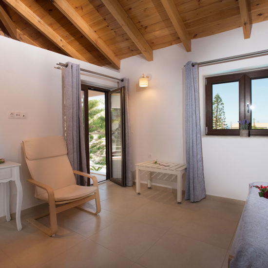 Bright bedroom with wooden vaulted ceiling, armchair, desk, and open balcony doors