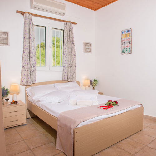 Bright double bedroom with a neatly made bed, floral curtains, bedside lamps and simple wall decor