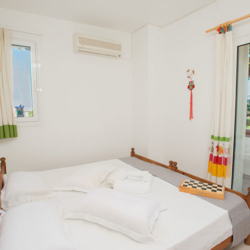 Bright twin bedroom with white bedding, wooden bed frames, and balcony doors beside a small window