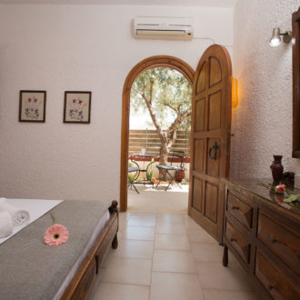 A traditional bedroom with wooden furniture opens through an arched door to a shaded private courtyard