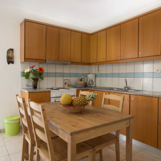 Bright apartment kitchen with wooden cabinets, a dining table, and an open doorway to the terrace