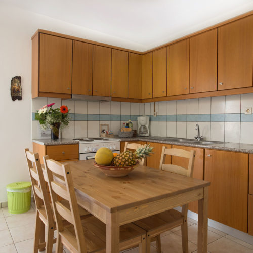 Bright apartment kitchen with wooden cabinets, a dining table, and an open doorway to the terrace