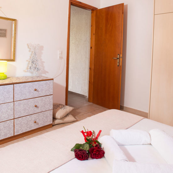 A neatly made bedroom with wardrobe, dresser, mirror, and folded towels at Houmeli Apartments in Kalamaki Crete