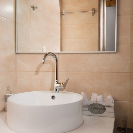 A modern bathroom sink with a round vessel basin, mirror, beige tile walls, and neatly folded towels