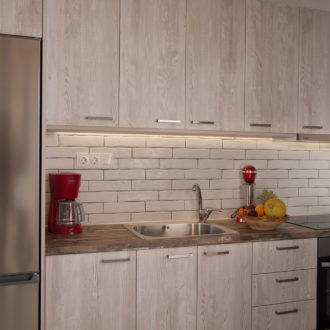 Compact kitchen with wood cabinetry, stainless steel appliances, a sink, and warm under-cabinet lighting