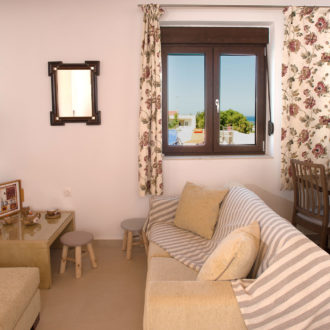 Bright living room with striped sofa, floral curtains, dining table, and a sea view through the window