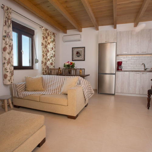 Open-plan living room with sofa, dining table, compact kitchen, and wooden ceiling in a bright apartment