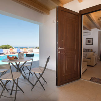 Covered terrace with outdoor table and chairs beside a pool, with the apartment entrance open to the interior
