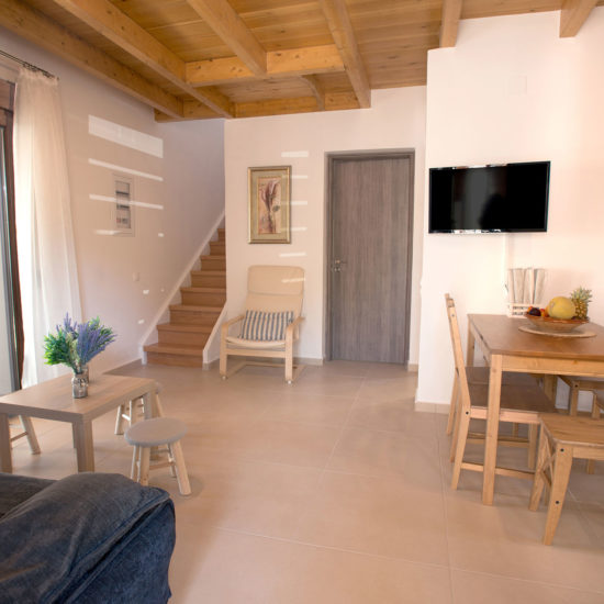 Bright open-plan living and dining area with wooden beams, stairs, a sofa, TV, and dining table in Louisa Apartment