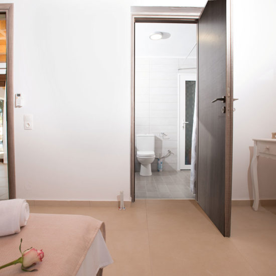 Bright ground-floor bedroom with an open bathroom doorway, mirror, and simple dressing table in Louisa apartment