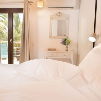 Bright bedroom with white bedding, wooden ceiling beams, a wall mirror, and balcony doors at Houmeli Apartments
