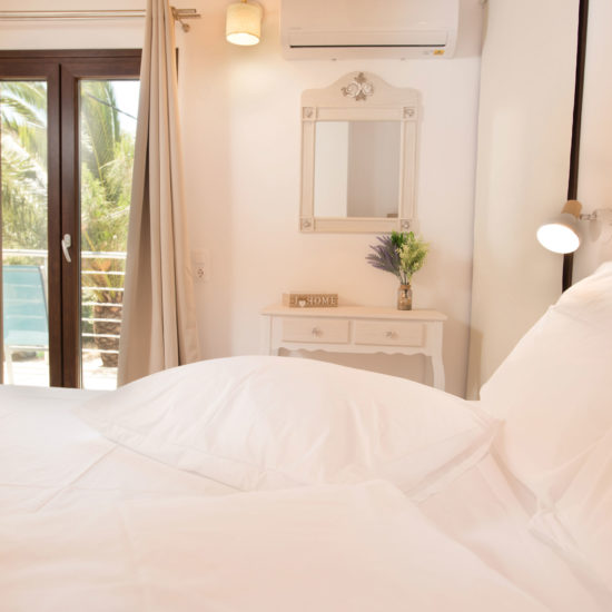 Bright bedroom with white bedding, wooden ceiling beams, a wall mirror, and balcony doors at Houmeli Apartments