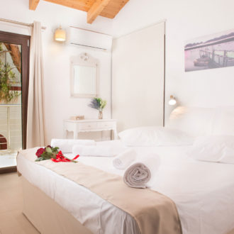 Bright first-floor bedroom with a double bed, balcony door, wooden ceiling beams, and soft neutral decor