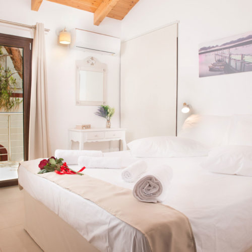 Bright first-floor bedroom with a double bed, balcony door, wooden ceiling beams, and soft neutral decor