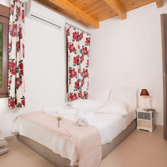A bright ground-floor bedroom with a double bed, floral curtains, wooden ceiling beams, and a window view