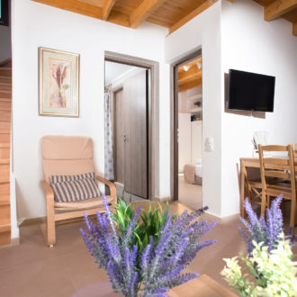 Bright maisonette interior with wooden stairs, a dining table, compact kitchen, and a cozy armchair at Houmeli Apartments