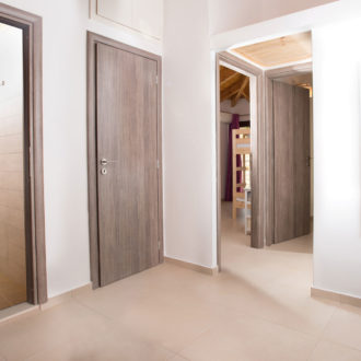 Bright upstairs hallway with wooden doors, tiled floors, and a bathroom entrance with a modern shower