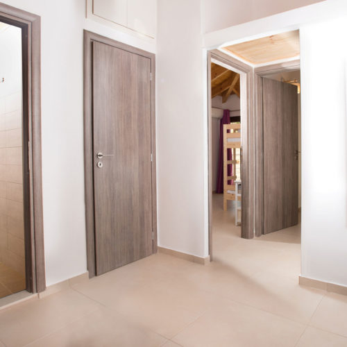 Bright upstairs hallway with wooden doors, tiled floors, and a bathroom entrance with a modern shower