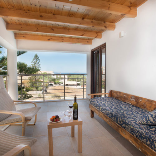 Covered balcony with lounge chairs, a wooden bench, and a sea view at Houmeli Apartments in Kalamaki Crete