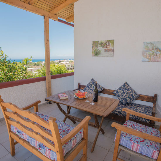 Covered terrace with wooden seating, a table setting, and sea views at Houmeli Apartments in Kalamaki Crete