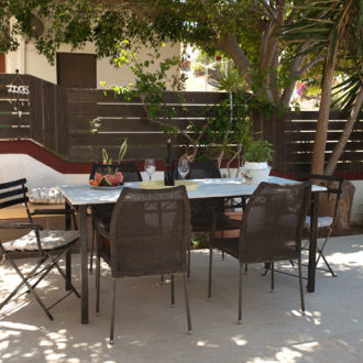 A shaded garden patio with a marble table, wicker chairs and dappled sunlight at Houmeli Apartments in Kalamaki Crete