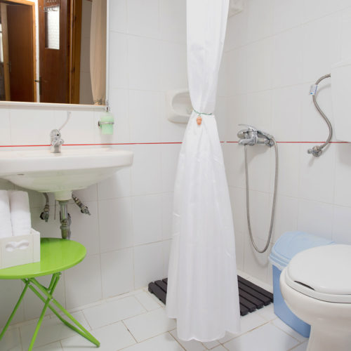 Compact bathroom with white tile, a shower curtain, sink, toilet, and small green side table