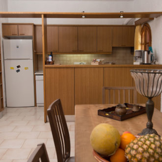 Wooden apartment kitchen with dining table, refrigerator, cabinets, and fruit on the table at Houmeli Apartments in Kalamaki Crete
