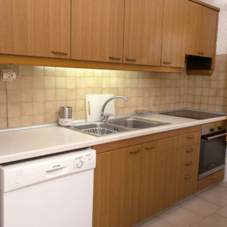 Compact kitchen with wooden cabinets, sink, stovetop, dishwasher and refrigerator in a family apartment