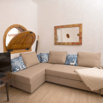 Cozy living room with a beige sectional sofa, TV, wooden accents, and decorative mirrors at Houmeli Apartments