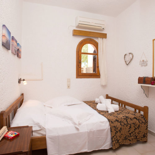 Twin bedroom with wooden beds, white bedding, a small arched window, and simple decorative touches