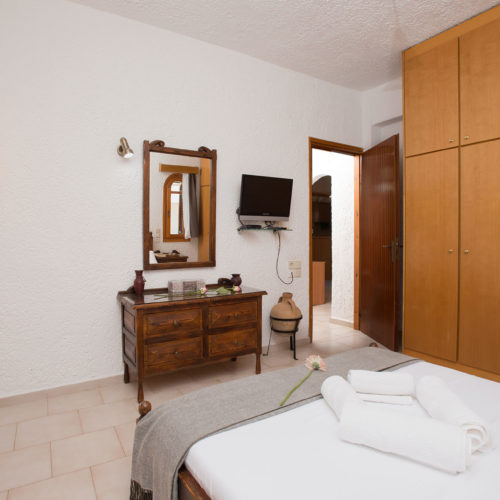 A traditional bedroom with wooden furniture, a wall mirror, wardrobe storage, and a neatly made bed