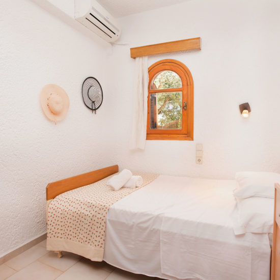 Bright twin bedroom with white walls, wooden furniture, and a small arched window bringing in daylight