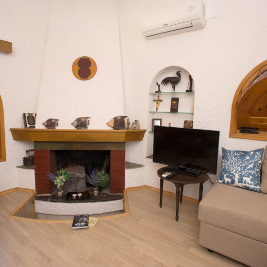 Cozy living room with fireplace, sofa, TV and arched wooden windows in a Kalamaki apartment