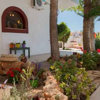 Courtyard garden with potted flowers, trees, stone accents, and a pool beside the Houmeli Apartments building