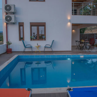 Courtyard pool beside Houmeli Apartments with lounge chairs, a covered seating area and evening lighting in Kalamaki, Crete