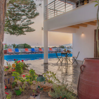 Courtyard pool area with sun loungers, a small table, potted plants, and warm sunset light at Houmeli Apartments