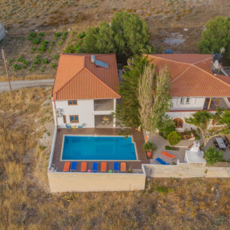 Aerial view of Houmeli Apartments with a pool, terracotta roofs, and dry countryside in Kalamaki, Crete
