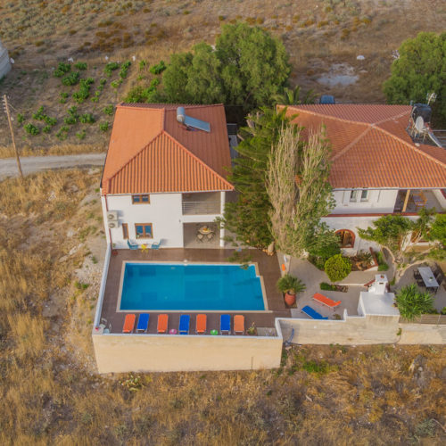 Aerial view of Houmeli Apartments with a pool, terracotta roofs, and dry countryside in Kalamaki, Crete