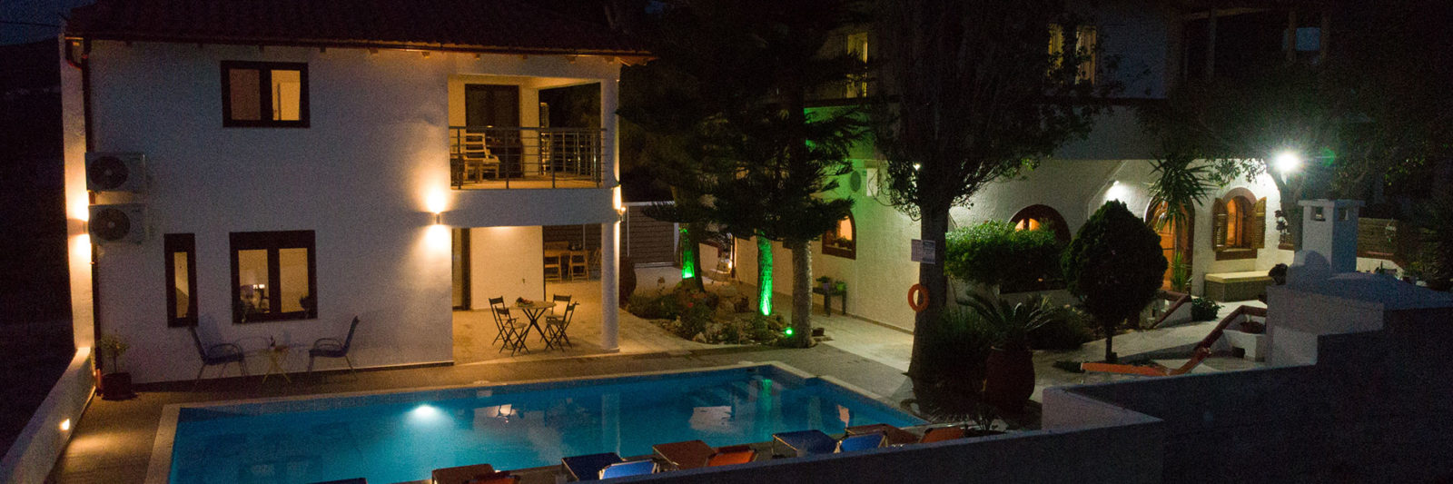Night view of Houmeli Apartments courtyard with illuminated pool and surrounding buildings