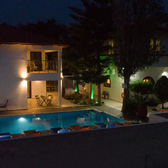 Night view of Houmeli Apartments courtyard with illuminated pool and surrounding buildings