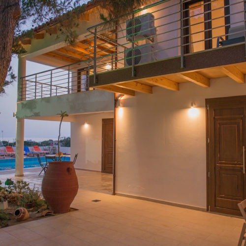 Courtyard view of Houmeli Apartments with poolside seating, balconies, and warm evening lighting in Kalamaki Crete