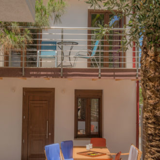 Shaded outdoor seating area with colorful chairs and a small table beside the Houmeli Apartments building in Kalamaki Crete