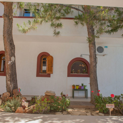 Shaded garden area with pine trees, arched windows, and white walls at Houmeli Apartments in Kalamaki Crete