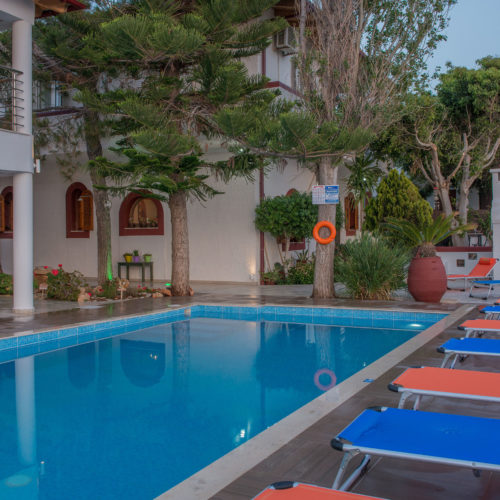 Outdoor pool at Houmeli Apartments with sun loungers, trees, and a calm courtyard setting in Kalamaki, Crete