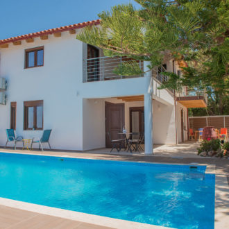 A bright courtyard at Houmeli Apartments in Kalamaki Crete with a swimming pool, sun loungers, and shaded seating