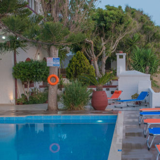 Poolside area with sun loungers, trees, and a small pool at Houmeli Apartments in Kalamaki, Crete