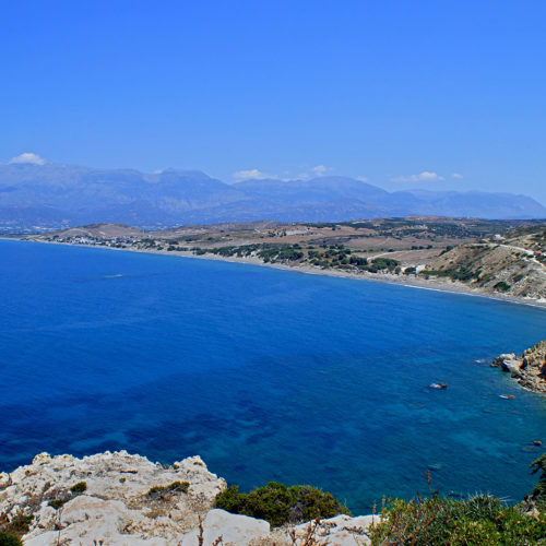 Panoramic view of Kommos beach with blue sea, rocky coastline, and distant mountains in Crete